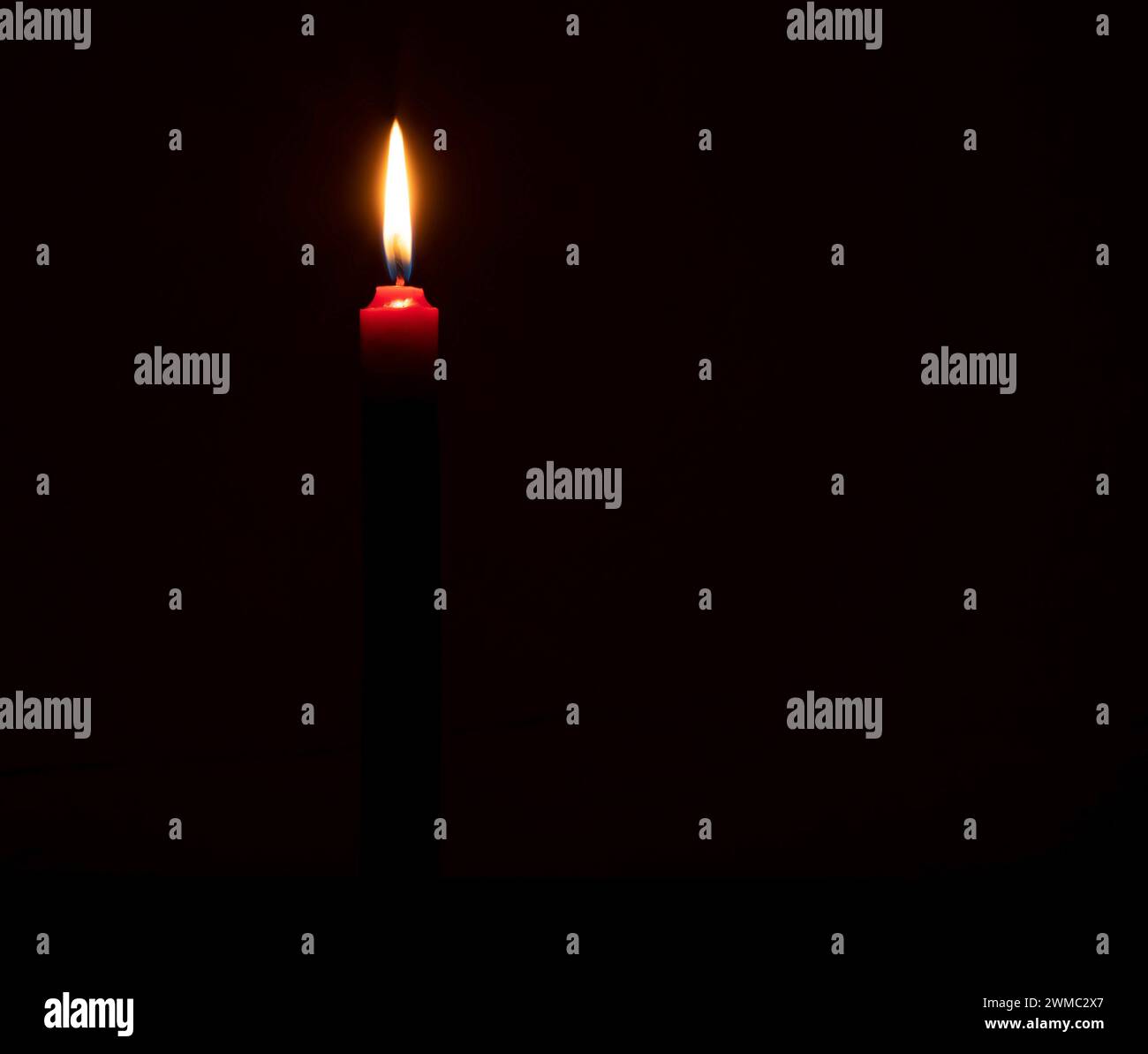 Una fiamma o una luce di una candela che brucia si illumina su una piccola candela rossa su sfondo nero o scuro sul tavolo in chiesa per Natale, funerale Foto Stock