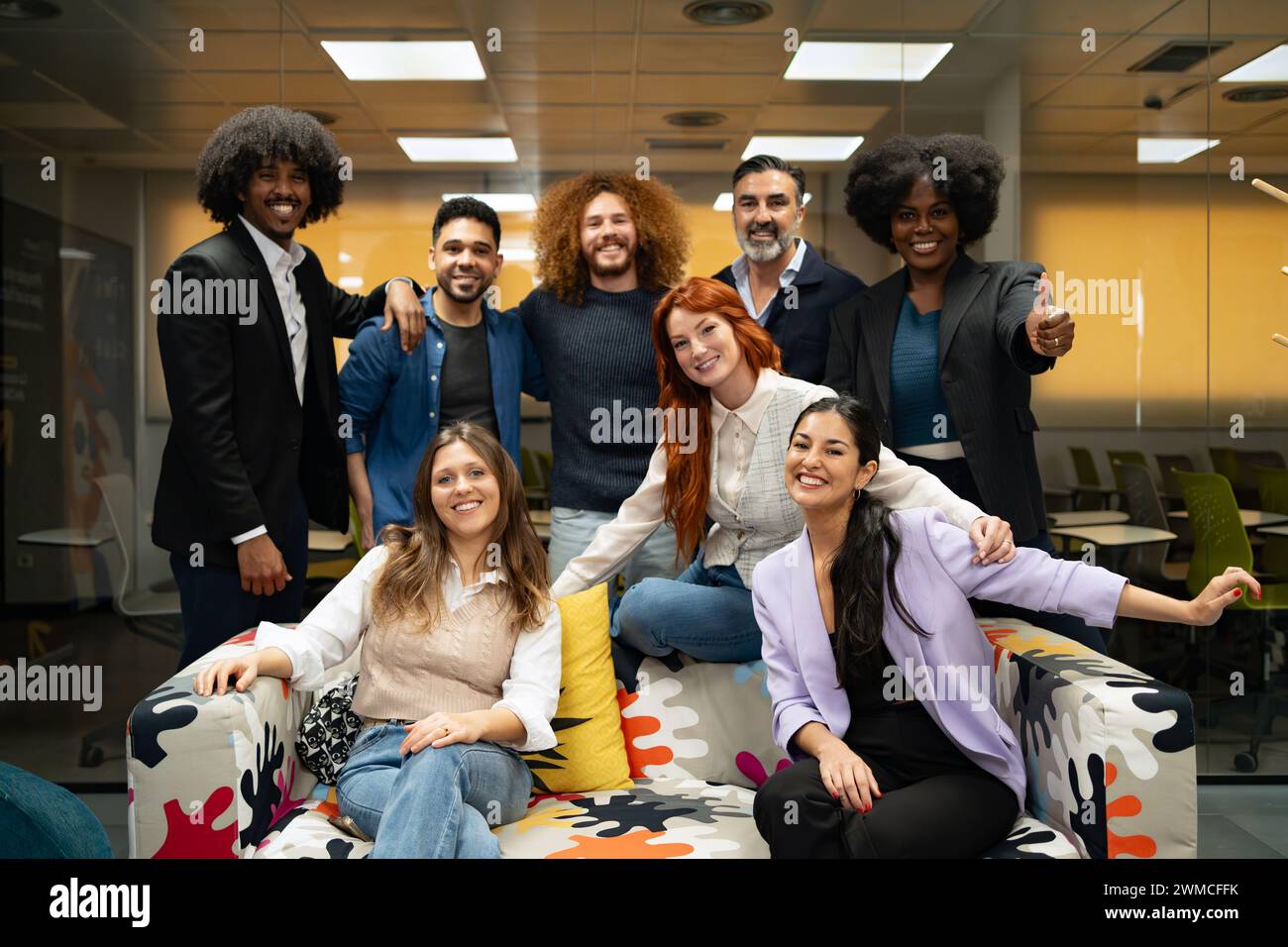 Un team diversificato di professionisti che festeggiano con le mani alzate in un ambiente d'ufficio allegro. Foto Stock