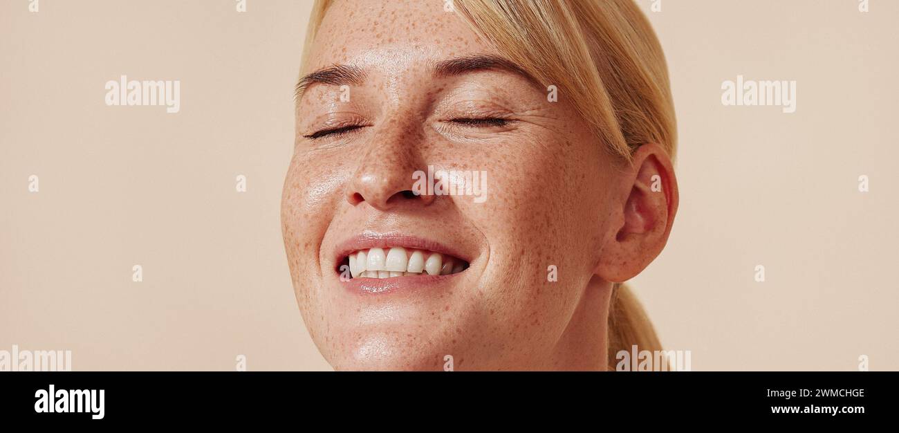 Ritratto dettagliato di una donna sorridente con lentiggini. Bionda felice con occhi chiusi e pelle lentigginita. Foto Stock