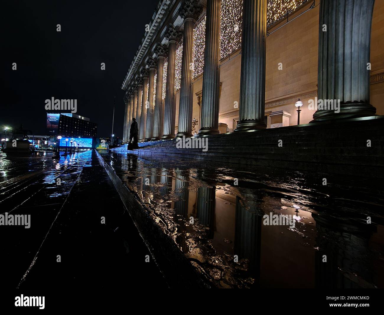 Un'accattivante vista notturna a Liverpool, con un luminoso cartellone e la dinamica vita di strada della città, con riflessi sulle superfici bagnate che creano un Foto Stock