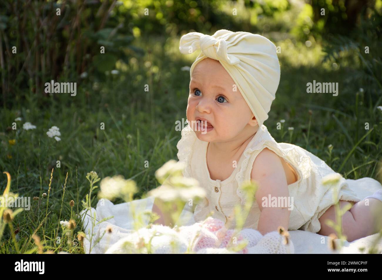 un bambino piccolo piange, disteso sullo stomaco su una coperta nel giardino sull'erba, in una passeggiata, Foto Stock