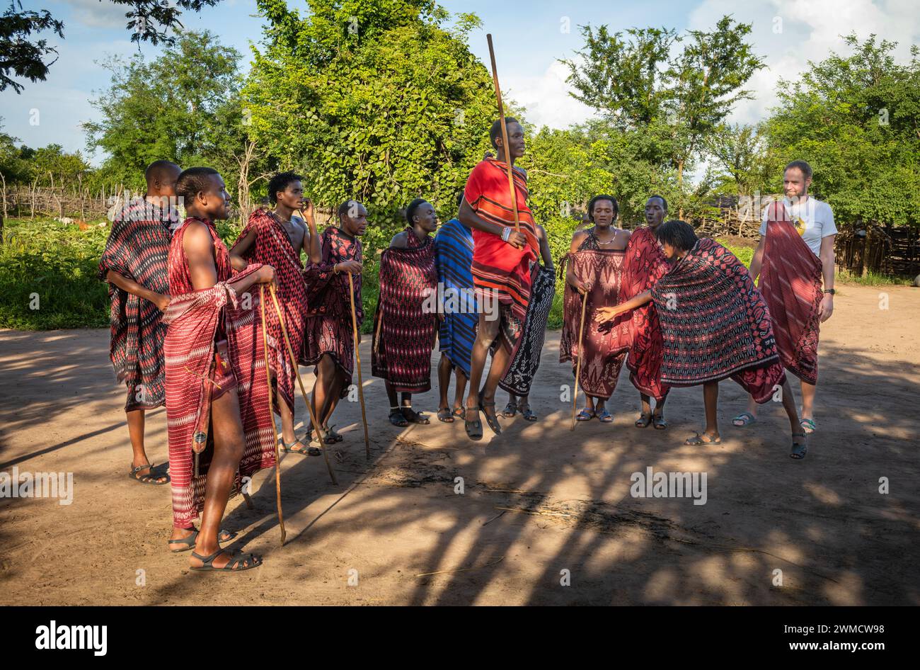 Un turista occidentale guarda un gruppo di guerrieri Maasai cantare e suonare la danza tradizionale del salto nel loro villaggio di Mikumi, Tanzania Foto Stock