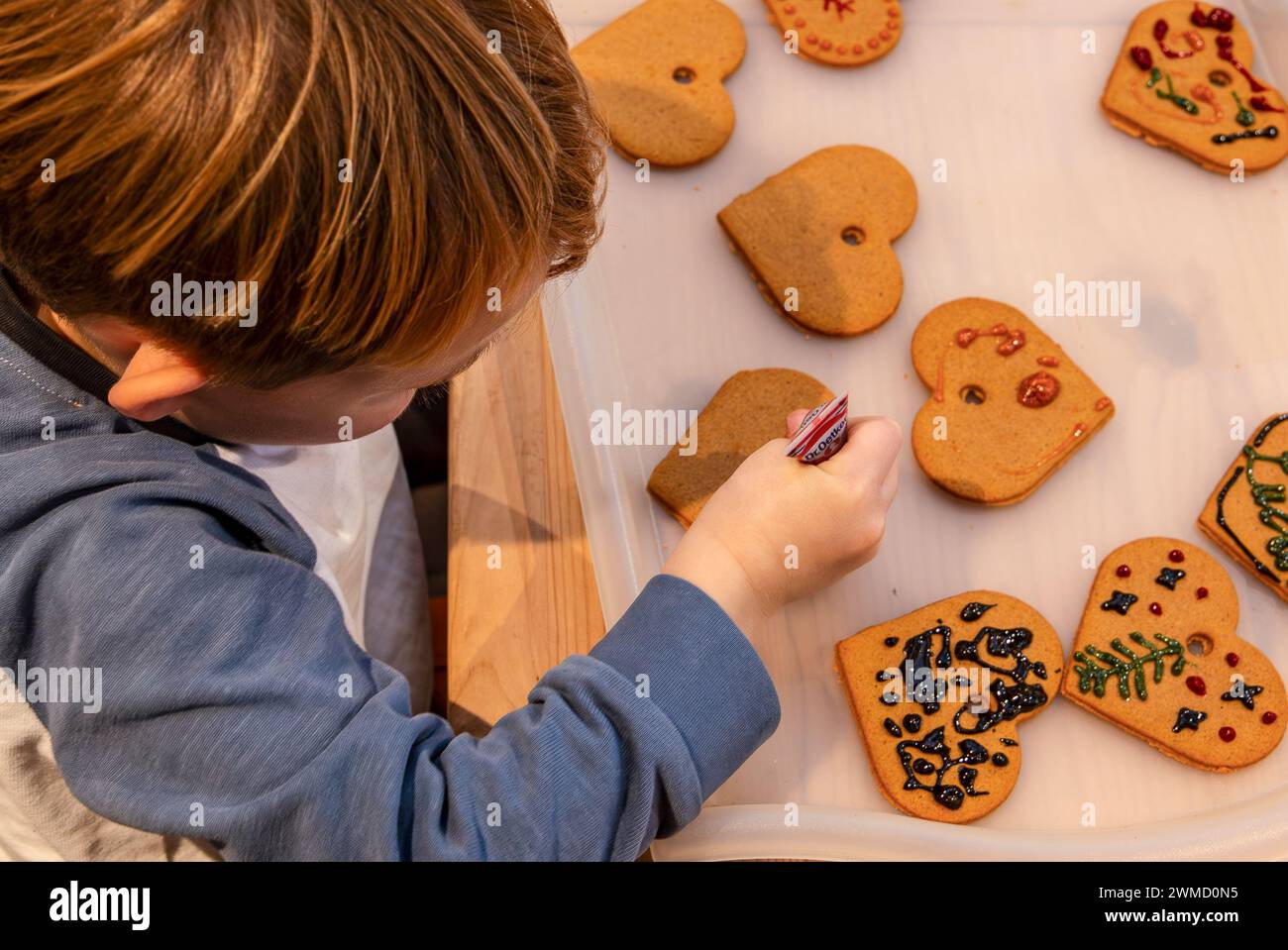 Bambino di 5 anni che decora biscotti a forma di cuore di pan di zenzero per Natale Foto Stock