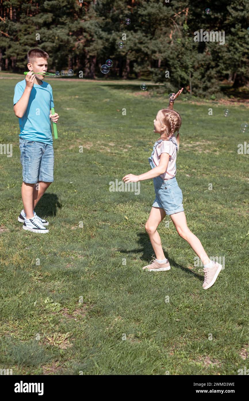 Due fratelli, un ragazzo più grande e una ragazza, giocano all'aperto su uno sfondo verde e soleggiato. Usato per l'assicurazione sanitaria per bambini e adolescenti e la vita sana. Foto Stock