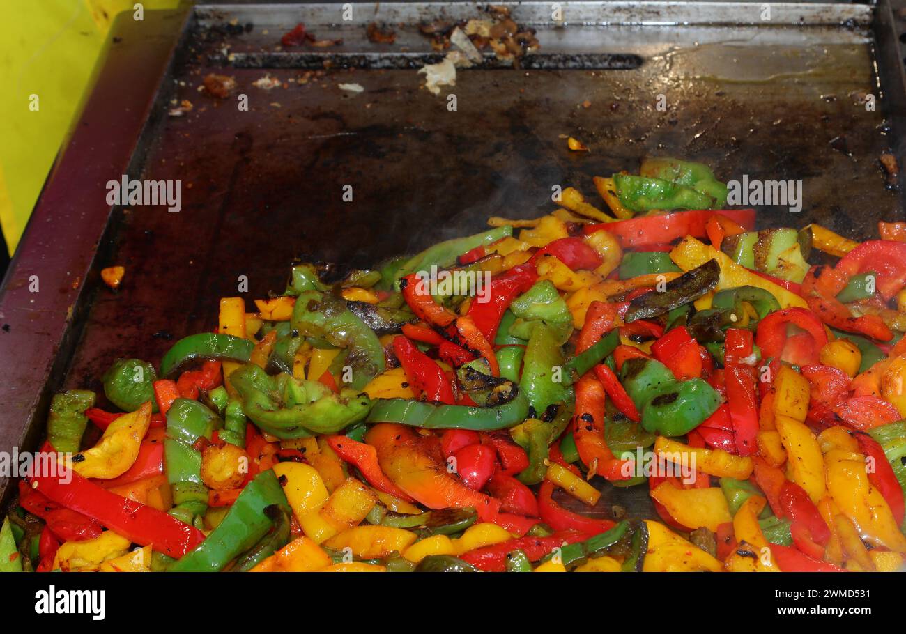 Peperoni gialli rossi e verdi sfrigolanti sulla piastra calda di un camion di cibo da strada che cucina con le spezie Foto Stock