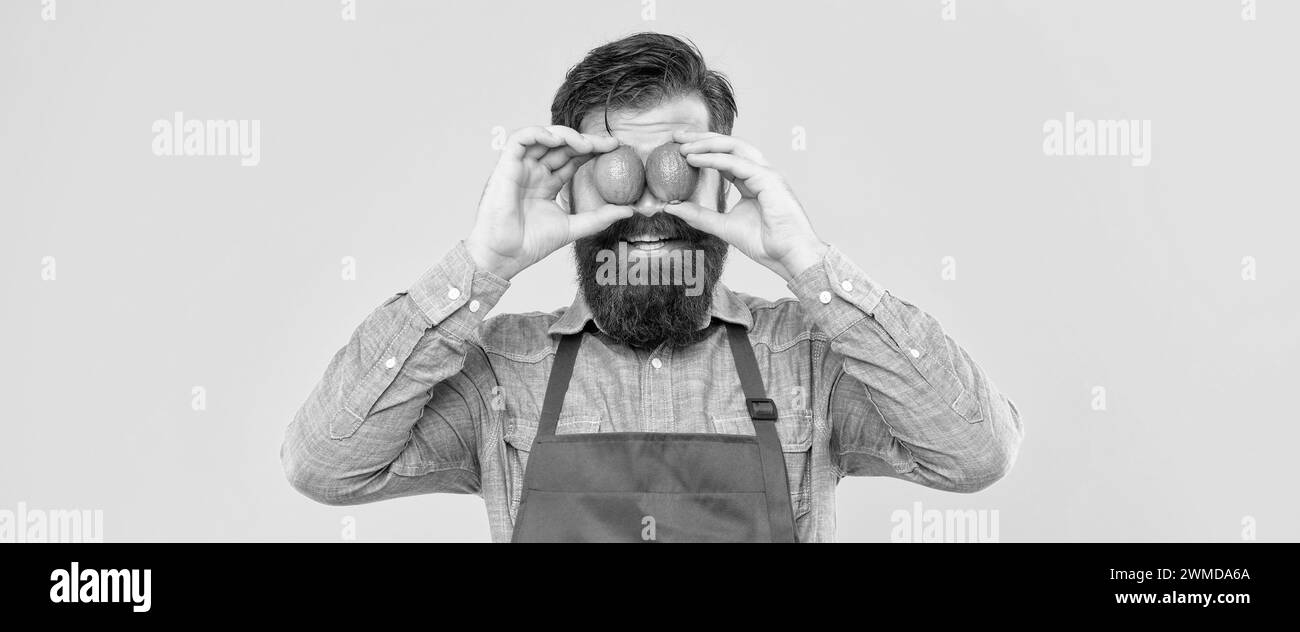 Uomo felice in grembiule che tiene fresco lime sugli occhi sfondo giallo, venditore di frutta Foto Stock