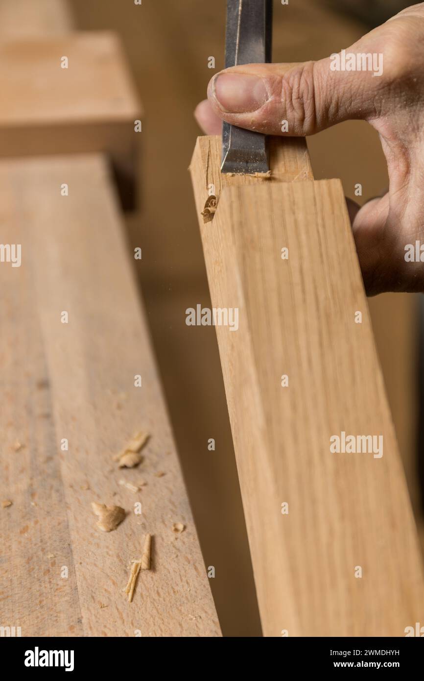 L'artigianato verticale focalizzato sulla fotografia è esposto mentre un falegname incide una tacca precisa in un pezzo di legno utilizzando uno scalpello affilato e mani stabili. Copia Foto Stock