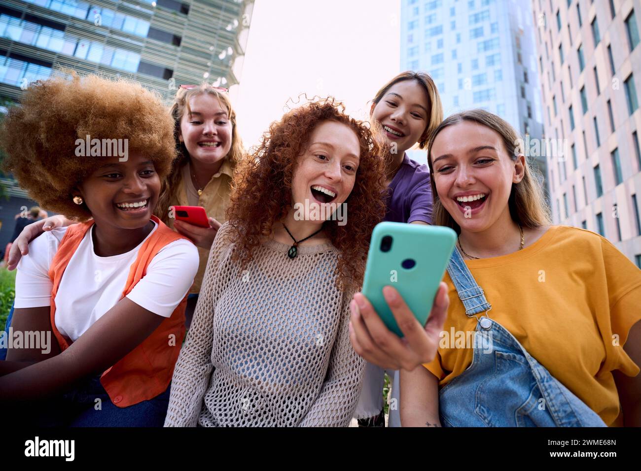 Giovani gruppi di persone gen z che si divertono a usare il cellulare insieme fuori. Felice comunità di studenti Foto Stock