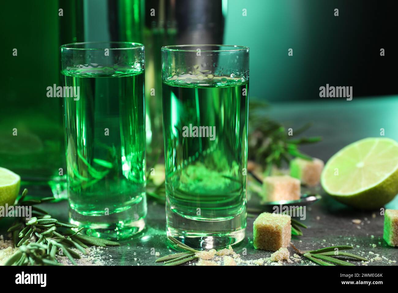 Absinthe in bicchieri da shot, zucchero di canna, rosmarino e lime su tavolo grigio, primo piano. Bevanda alcolica Foto Stock