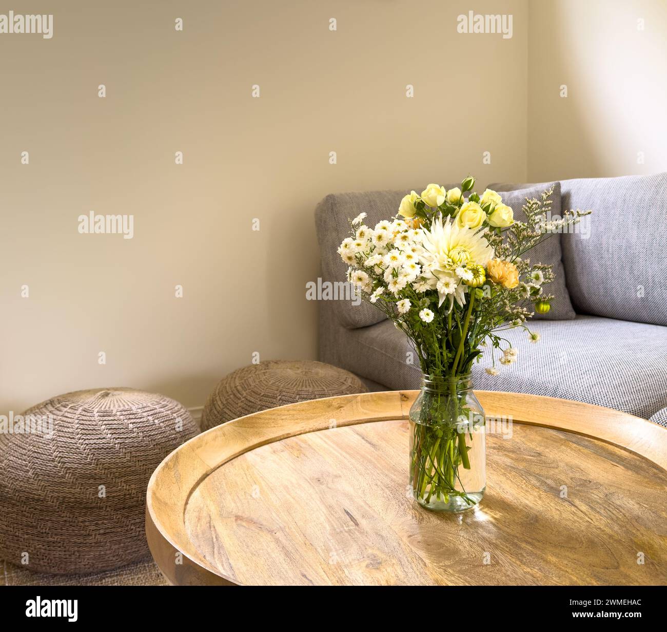 Fiori freschi tagliati in un barattolo su un tavolino rotondo in legno in una sala lounge Foto Stock