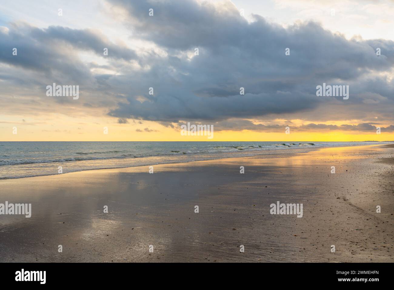 Il tramonto dipinge il cielo con tonalità calde su una spiaggia tranquilla. Foto Stock