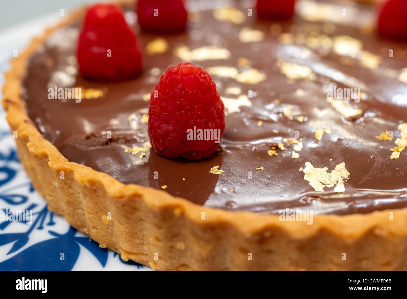 Torta al cioccolato con marmellata di albicocche decorata con lamponi freschi e targhe d'oro 24 carati su lavagna bianca blu Foto Stock