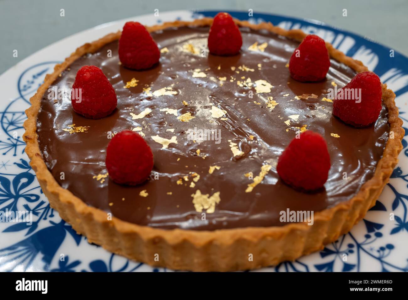 Torta al cioccolato con marmellata di albicocche decorata con lamponi freschi e targhe d'oro 24 carati su lavagna bianca blu Foto Stock