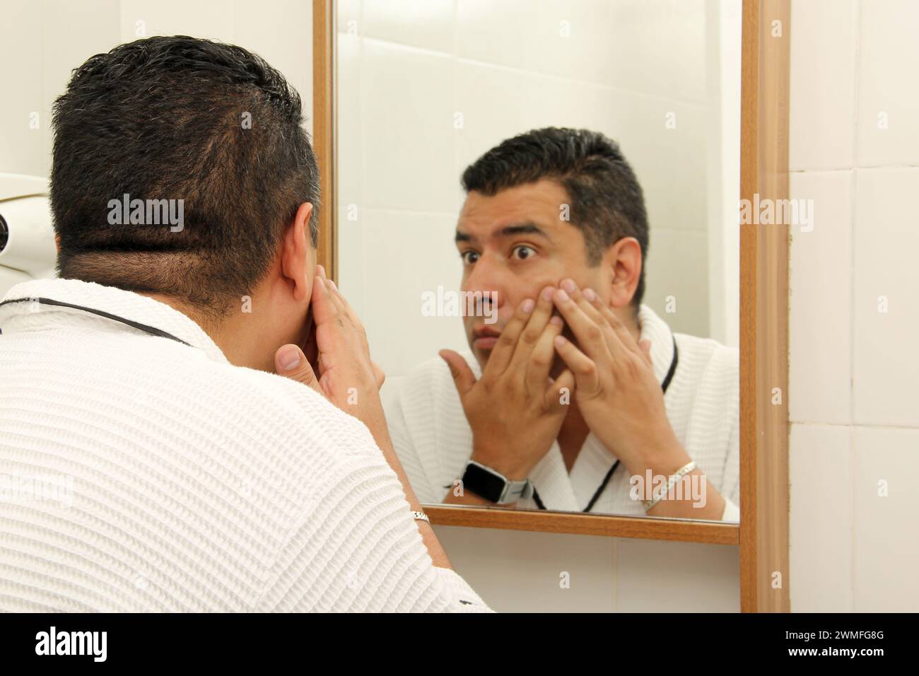 L'uomo latino di 40 anni dalla pelle scura si prende cura della pelle al mattino e di notte con siero, crema e protettore per evitare macchie e rughe Foto Stock