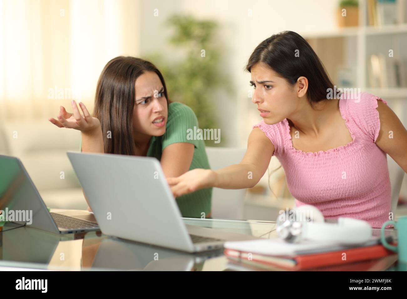 Due studenti arrabbiati che discutono di studiare online con i notebook a casa Foto Stock