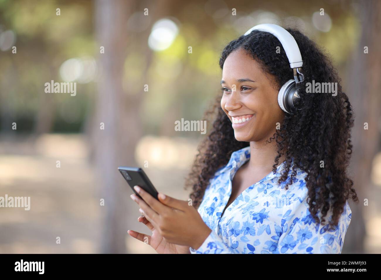 Donna nera felice che indossa le cuffie che ascolta musica che tiene il telefono all'esterno Foto Stock