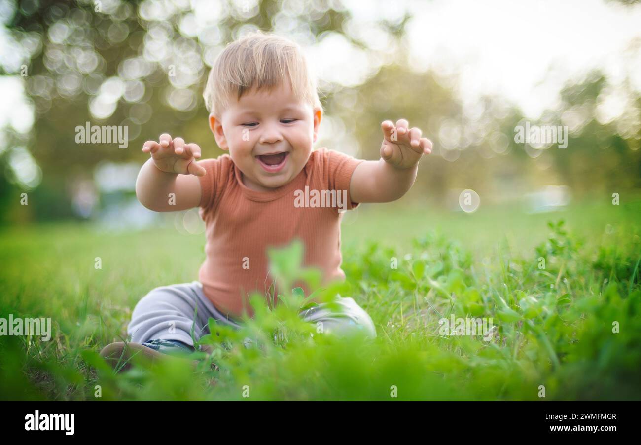 Il bambino che ride si diverte seduto sull'erba durante il giorno di sole. Ora legale, bambino felice Foto Stock