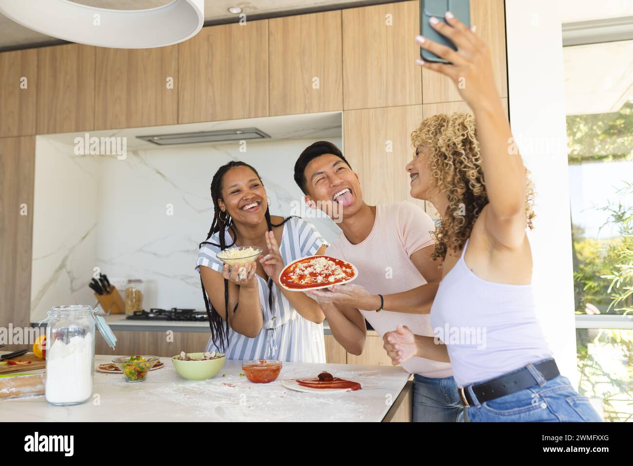 Il giovane asiatico e due giovani donne birazziali si divertono a fare la pizza a casa Foto Stock