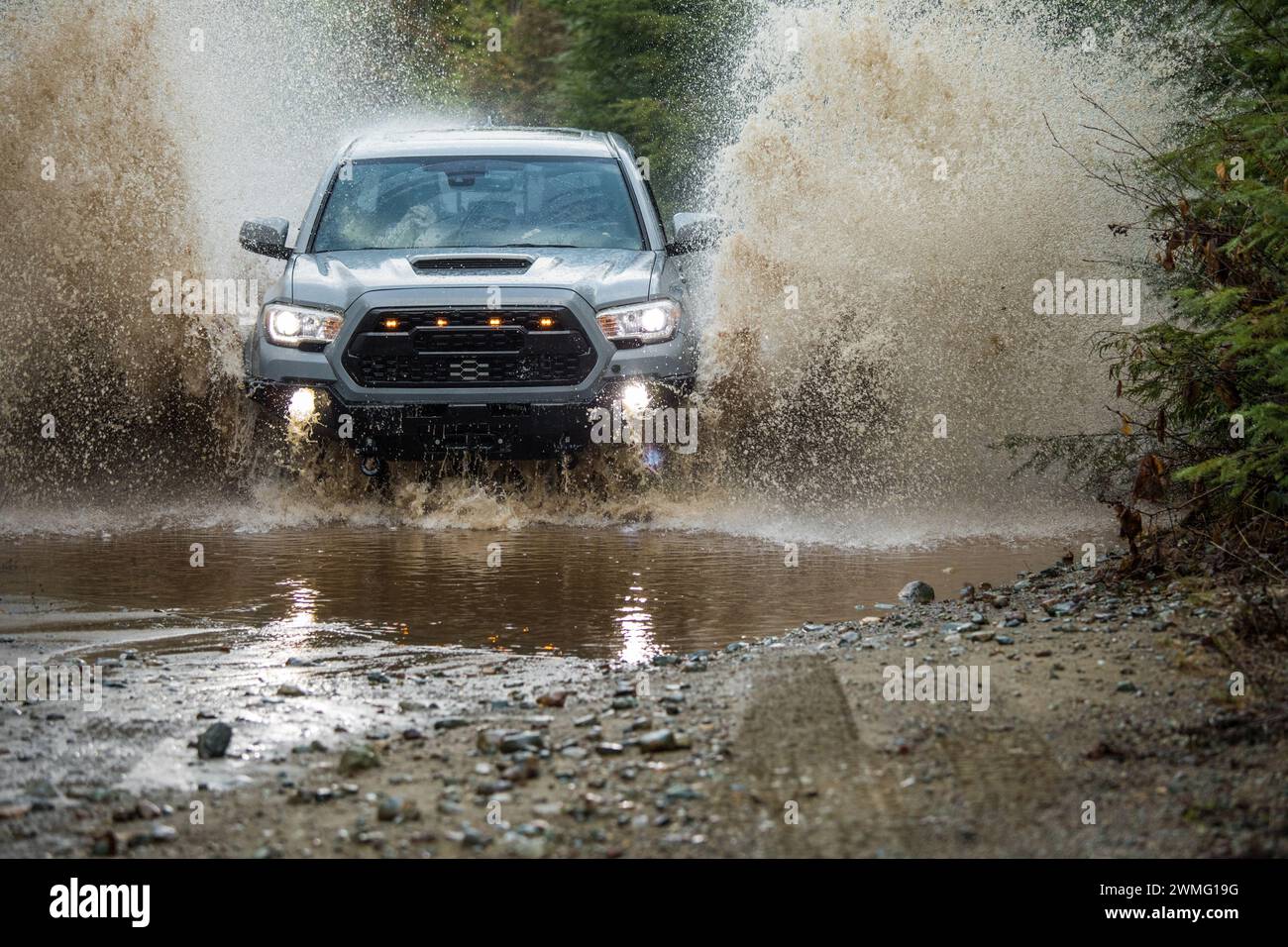 veicolo 4x4 che guida su una strada ghiaiosa allagata, spruzzi d'acqua nell'aria Foto Stock