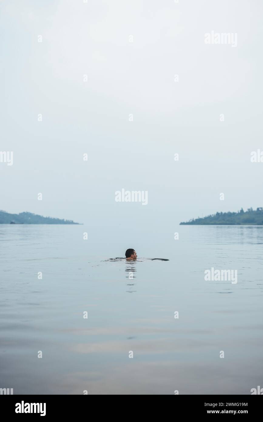 L'uomo nuota nelle tranquille acque del lago Kivu, Ruanda Foto Stock
