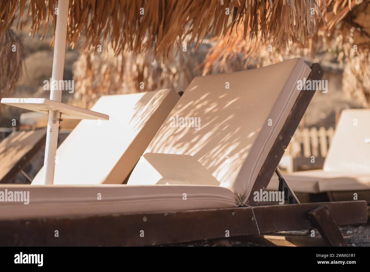 Primo piano di sedie a sdraio con ombrelloni di paglia sotto il sole caldo Foto Stock