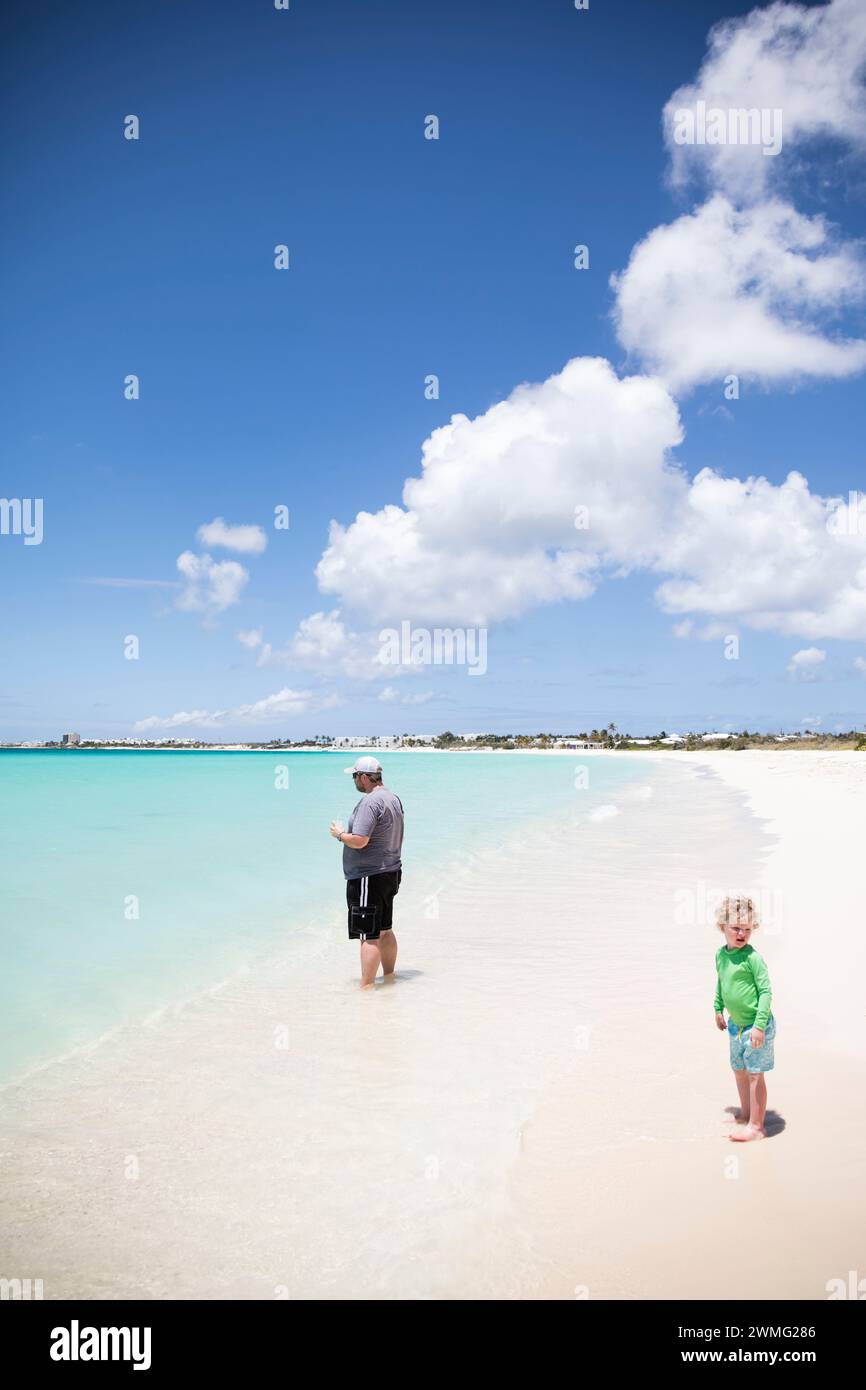 Uomo con bevande in piedi accanto al bambino sulla spiaggia dei Caraibi Foto Stock