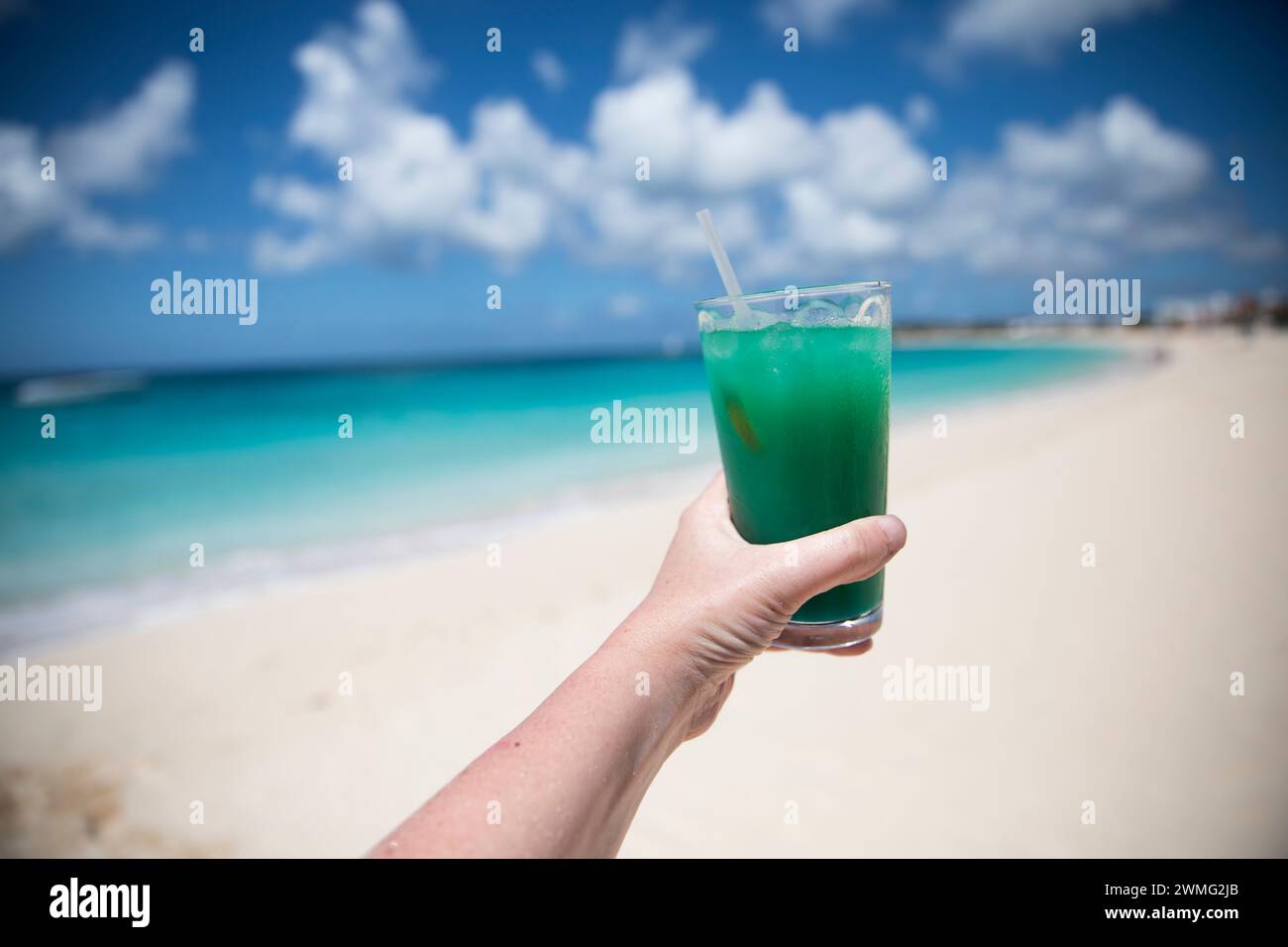 Le mani senza volto tengono bevande tropicali contro il cielo blu sulla spiaggia dei Caraibi Foto Stock