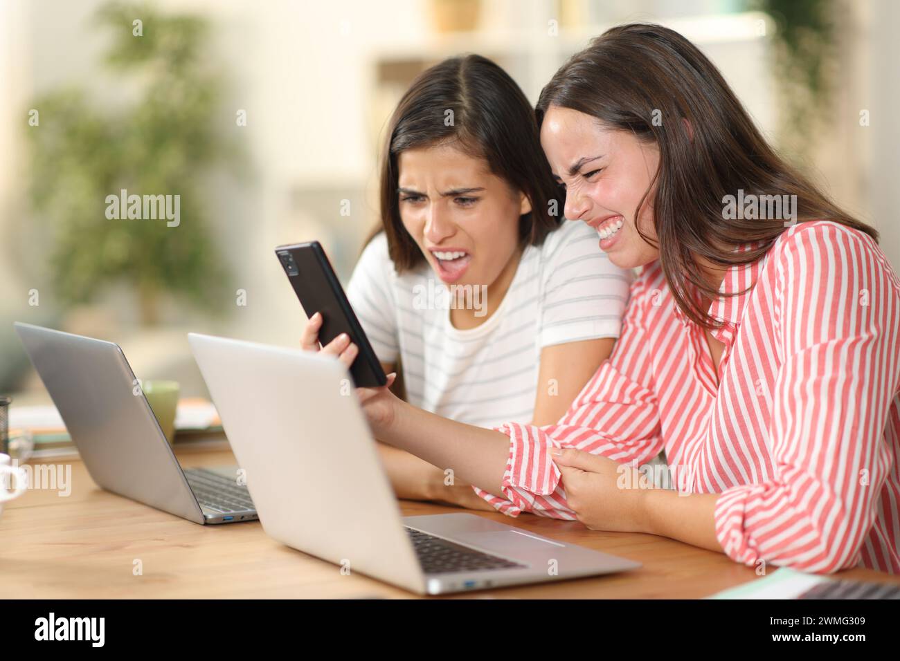 Due donne disgustate che controllano i contenuti brutti sul telefono a casa Foto Stock
