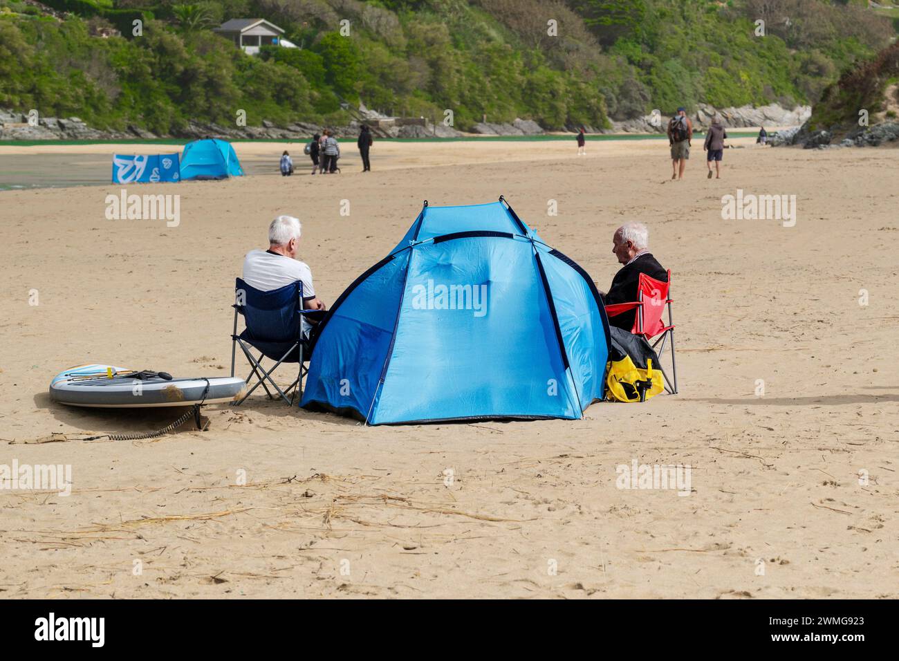 Due uomini maturi seduti con il loro rifugio blu sulla spiaggia di Crantock Beach a Newquay, in Cornovaglia, nel Regno Unito. Foto Stock