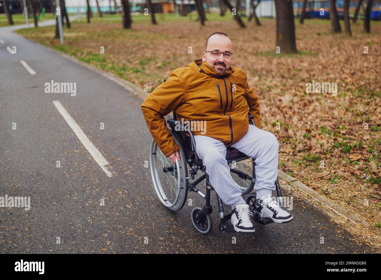 Ritratto di un uomo paraplegico in sedia a rotelle nel parco. Sta rotolando sulla strada. Foto Stock