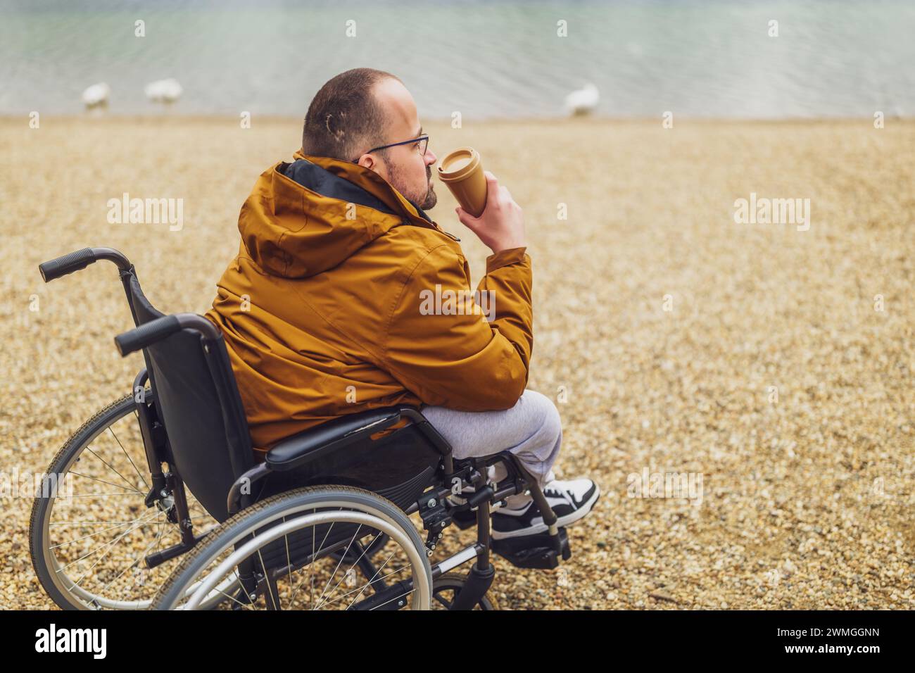 Un portatore di handicap paraplegico in sedia a rotelle si sta godendo all'aperto e bevendo un caffè. Foto Stock
