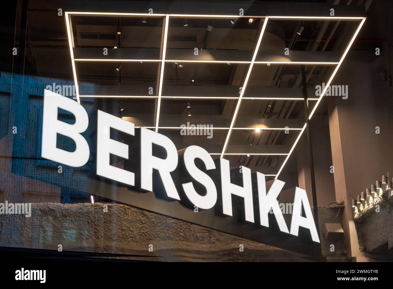 Angolo basso del cartello Bershka collocato nell'edificio del negozio di abbigliamento per le informazioni dei clienti davanti con lettere bianche luminose sotto le lampade in d Foto Stock