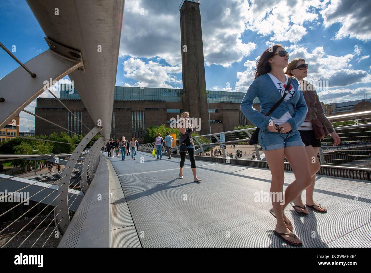 Due giovani donne che attraversano il Millennium Bridge con sullo sfondo la Tate Modern Art Gallery . Southbank, Londra, Regno Unito Foto Stock