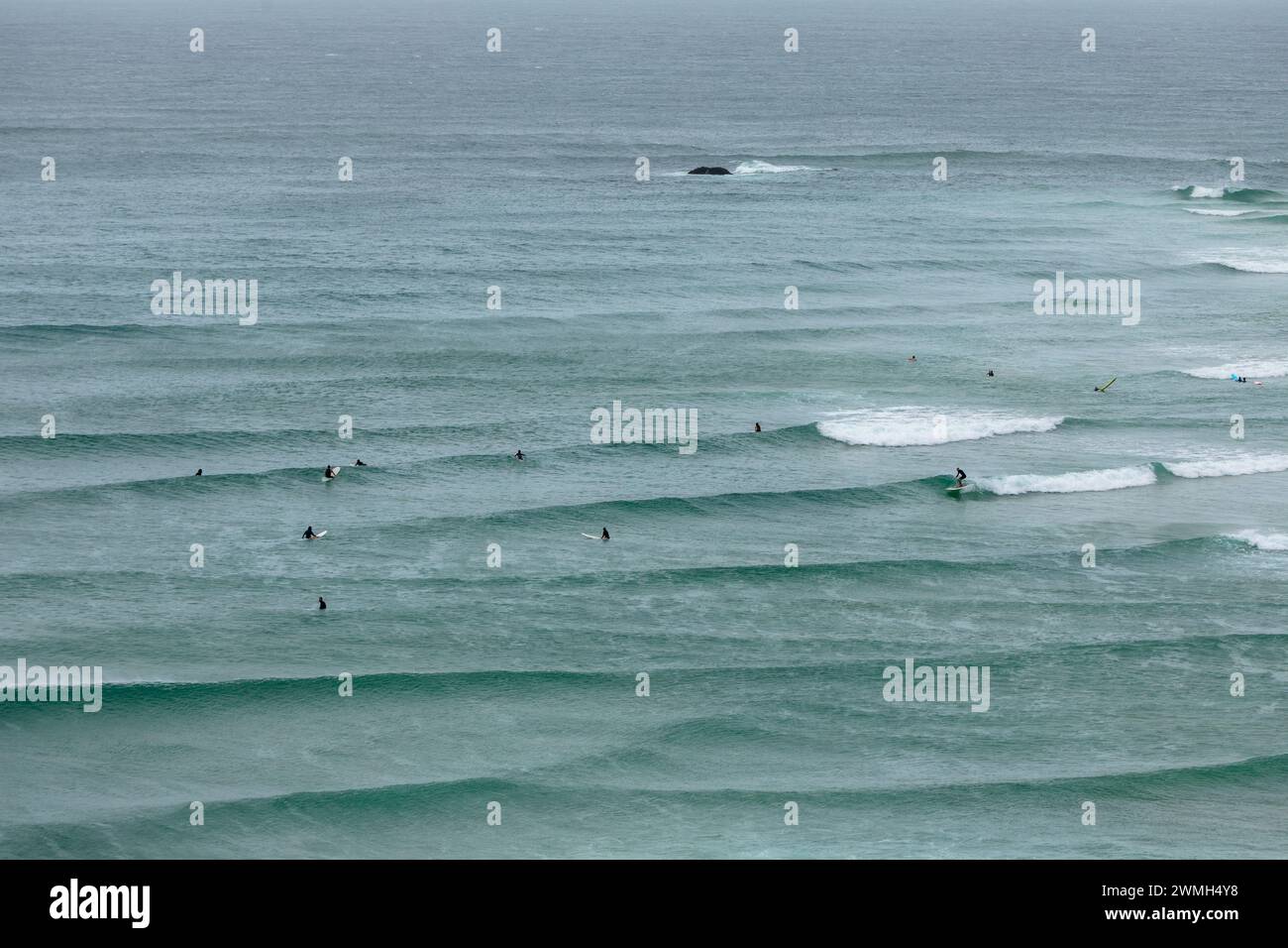 I surfisti attraversano le onde dell'Oceano Pacifico al largo di Capo Byron, vicino al punto più orientale della terraferma australiana. Foto Stock