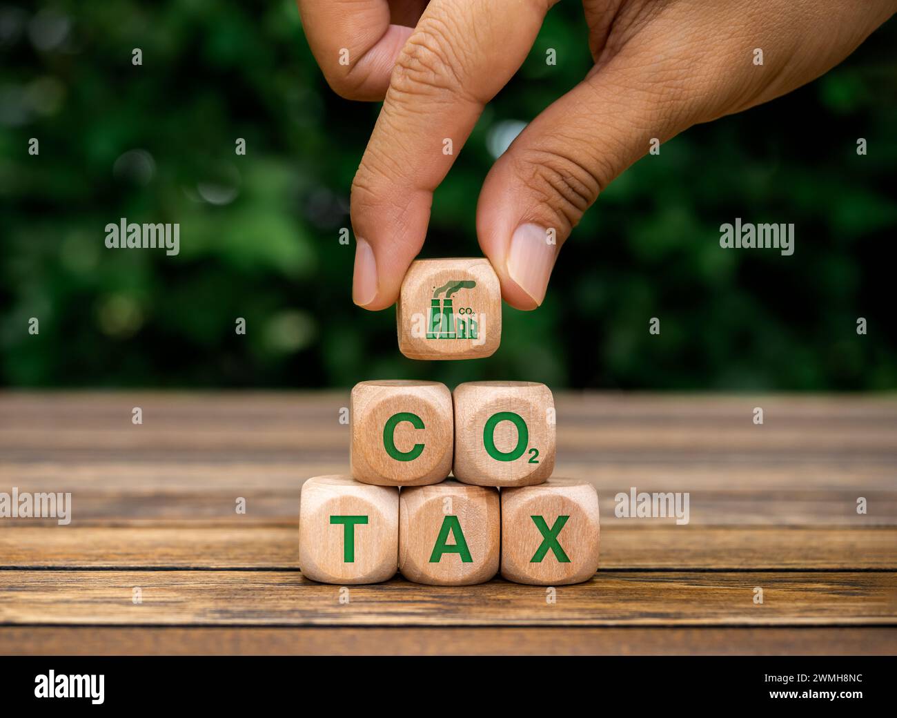 Tassa sul carbonio. Icona della fabbrica di fumo in mano, metti sopra la piramide di blocchi di legno a forma di cubo con testo verde, TASSA CO2 sulla scrivania di legno. Ambientale, sociale Foto Stock