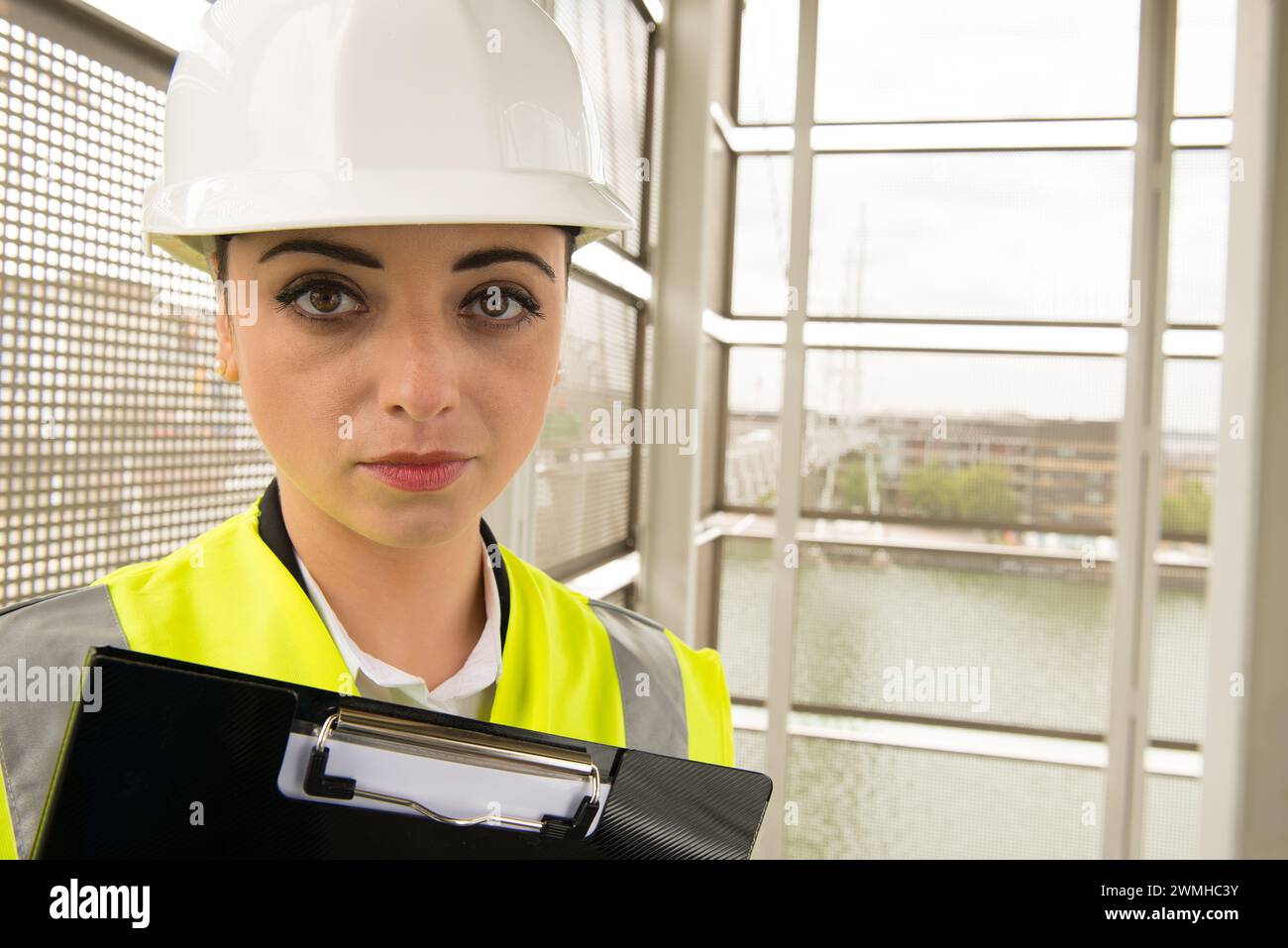 Giovane donna che lavora nel settore ingegneristico, indossa casco di sicurezza bianco e giubbotto ad alta visibilità. Foto Stock