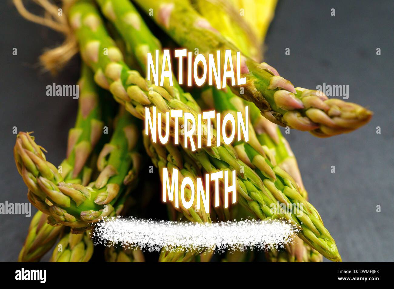 National Nutrition Month, con un pacchetto di asparagi freschi legati con spago su una lavagna di ardesia, accompagnati da testo colorato. Foto Stock