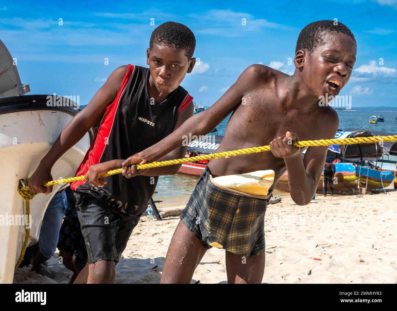 Due giovani ragazzi si trascinano su una corda per portare una barca a riva sulla spiaggia di Stone Town, Zanzibar, Tanzania. Foto Stock