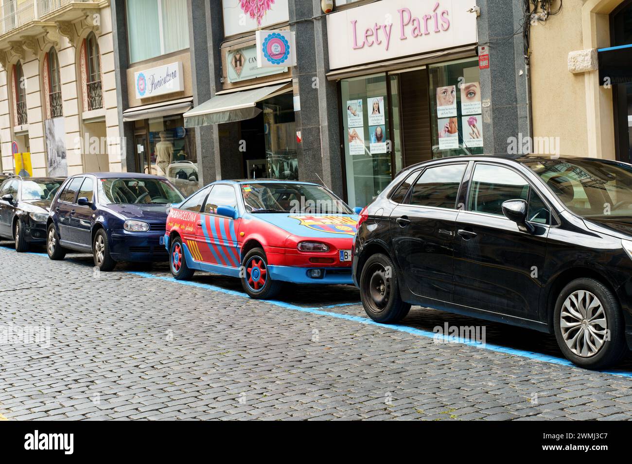 Figueres, Spagna - 14 maggio 2023: Una vivace auto rossa e blu, decorata con il logo del FC Barcelona e i temi di design, è parcheggiata dal marciapiede su un urba Foto Stock Figueres, Spagna - 14 maggio 2023: Una vivace auto rossa e blu, decorata con il logo del FC Barcelona e i temi di design, è parcheggiata dal marciapiede su un urba Foto Stock