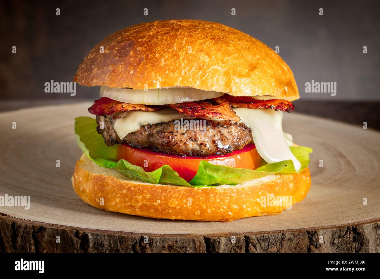 cheeseburger fatto in casa con lattuga fresca pomodoro cipolla pancetta croccante hamburger di manzo succoso e formaggio fuso in un panino servito su un vassoio di legno naturale Foto Stock