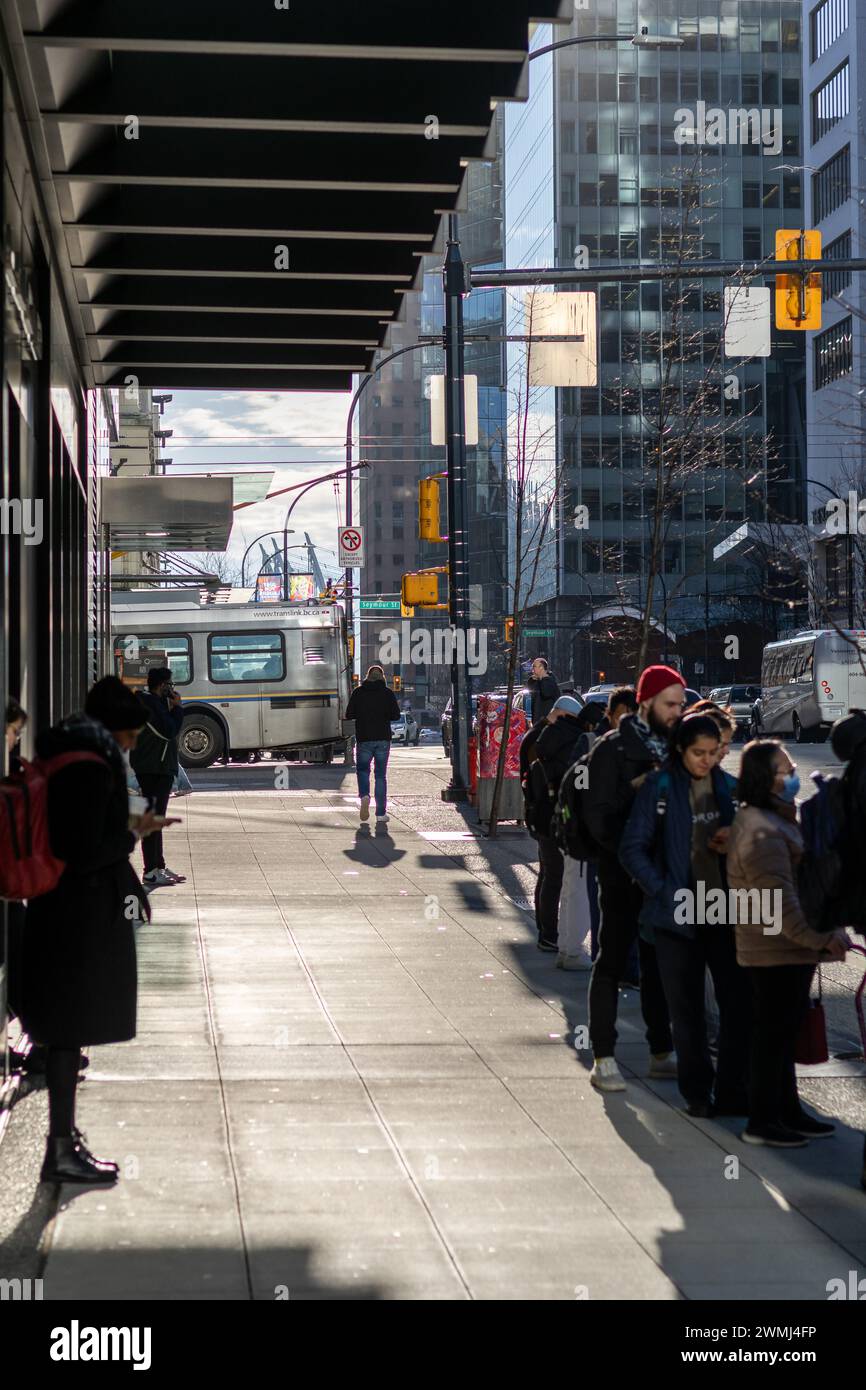 Una vista del marciapiede di Georgia Street che guarda a est, mostrando le persone in attesa in coda alla fermata dell'autobus. Un autobus sulla strada è visibile sullo sfondo. Foto Stock