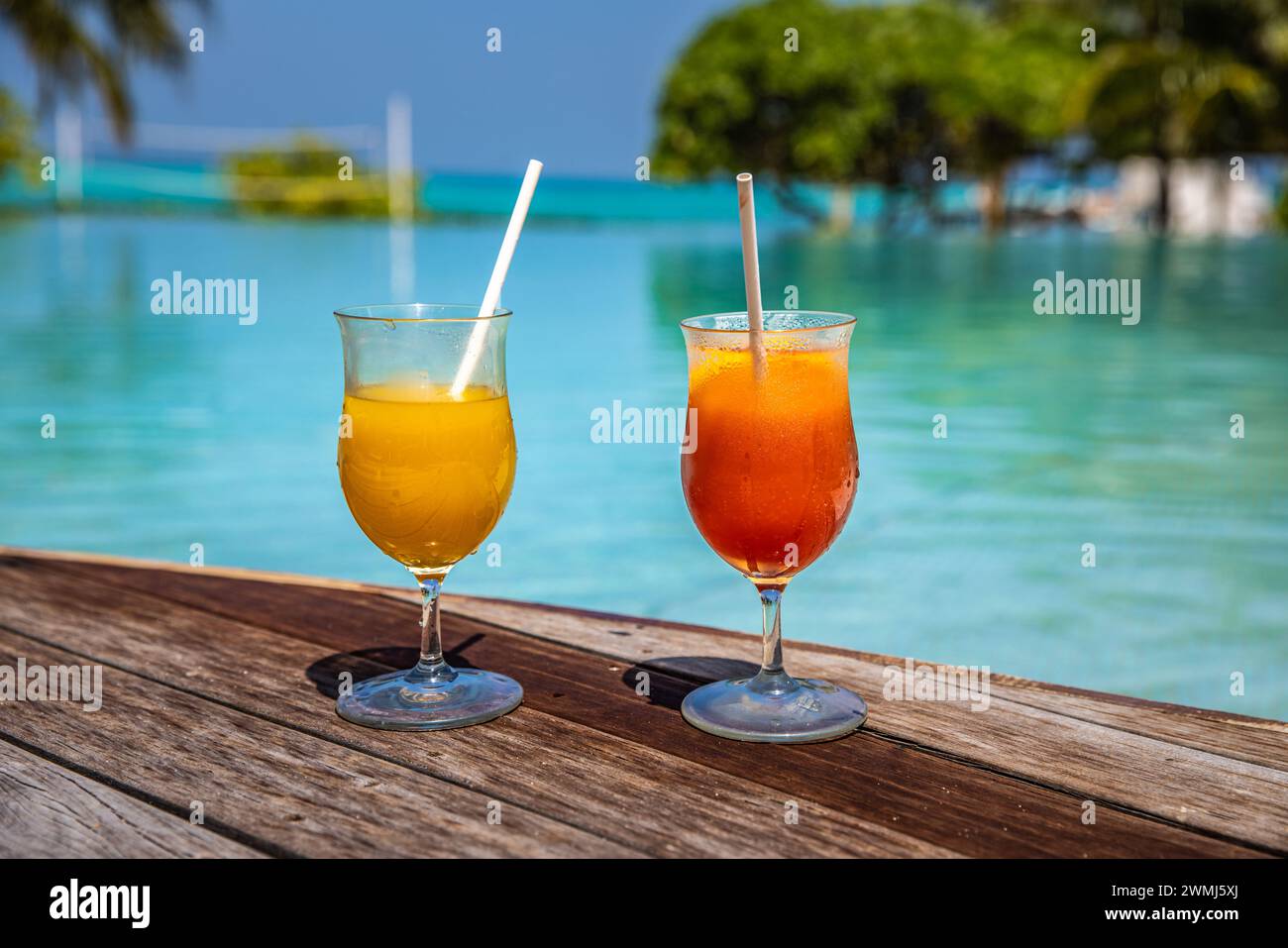 Cocktail colorati serviti in un lussuoso resort tropicale alle Maldive. A bordo piscina con palme e lettini sfocati e luce solare. Colori luminosi e solari Foto Stock