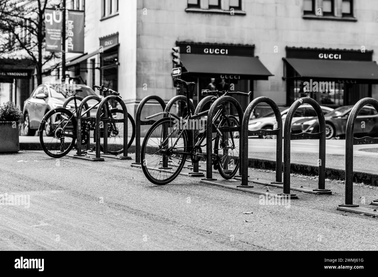 Vancouver, Canada - 15 febbraio 2024: Una foto in bianco e nero di un paio di biciclette parcheggiate su Hornby Street con auto e un negozio Gucci sullo sfondo. Foto Stock