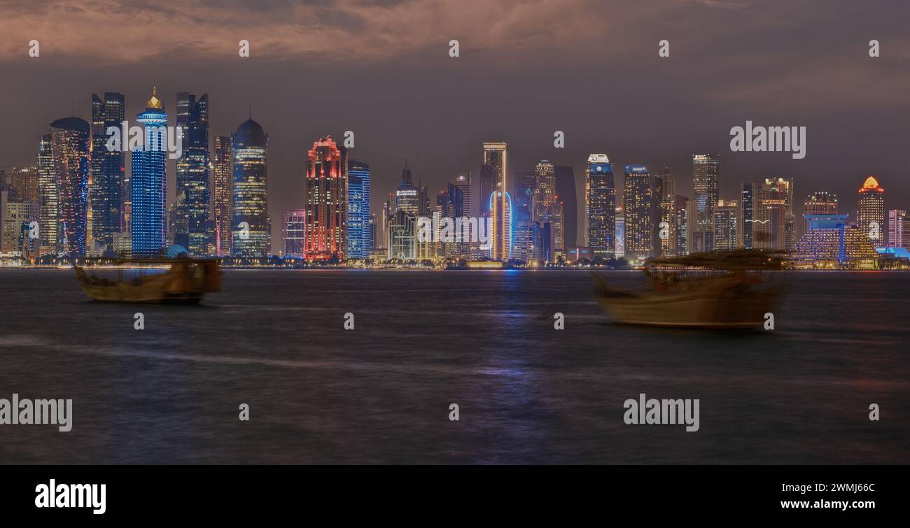 Doha, skyline del Qatar di notte con dhow e barche nel golfo arabo Foto Stock