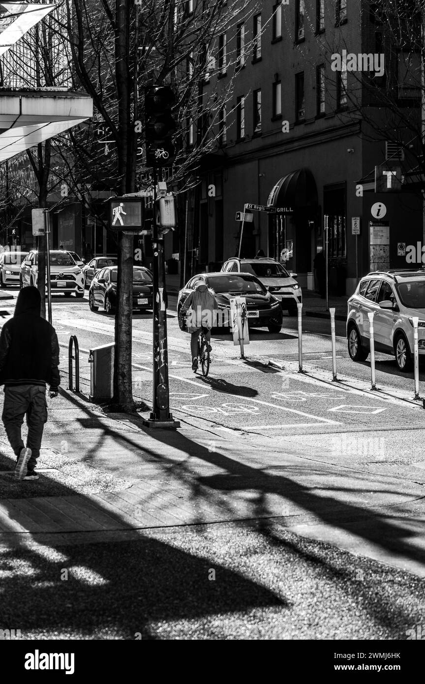 Vancouver, Canada - 16 febbraio 2024: Una foto in bianco e nero di una donna in bicicletta sulla pista ciclabile di Dunsmuir Street, pedalando in salita. Foto Stock