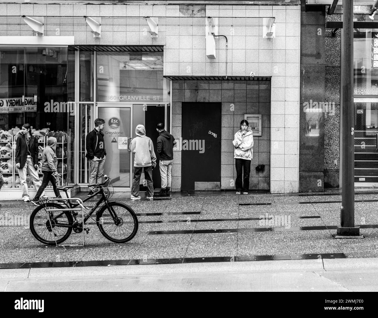 Vancouver, Canada - 21 febbraio 2024: Una scena in bianco e nero di studenti che fanno una pausa fuori da un college in Granville Street. Una donna sta svapando. Foto Stock