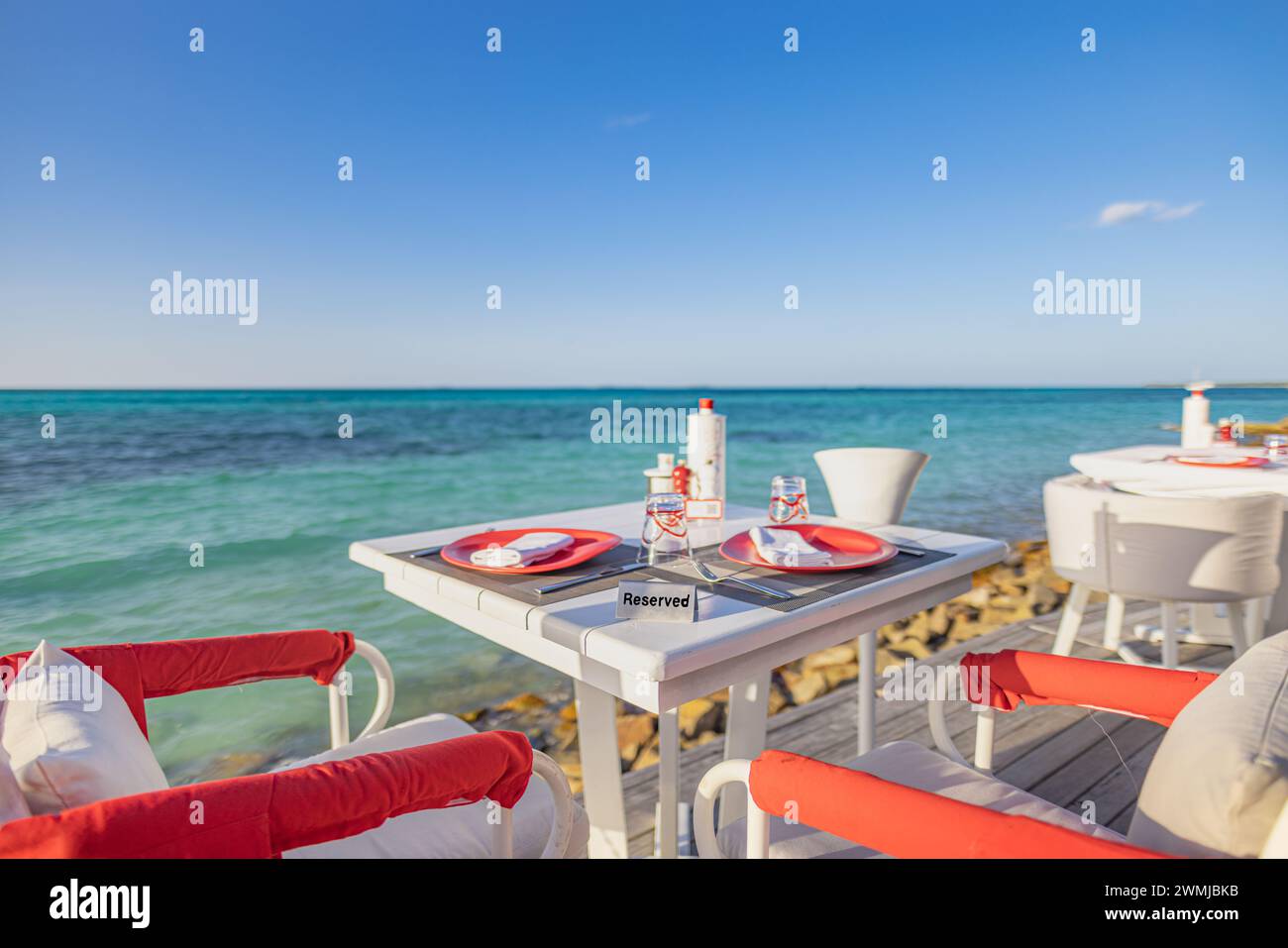 Rilassante ristorante all'aperto sulla spiaggia. Tavolo al ristorante sulla spiaggia tropicale. Eleganti tavoli e sedie in legno bianco sotto una bella luce soffusa del sole Foto Stock