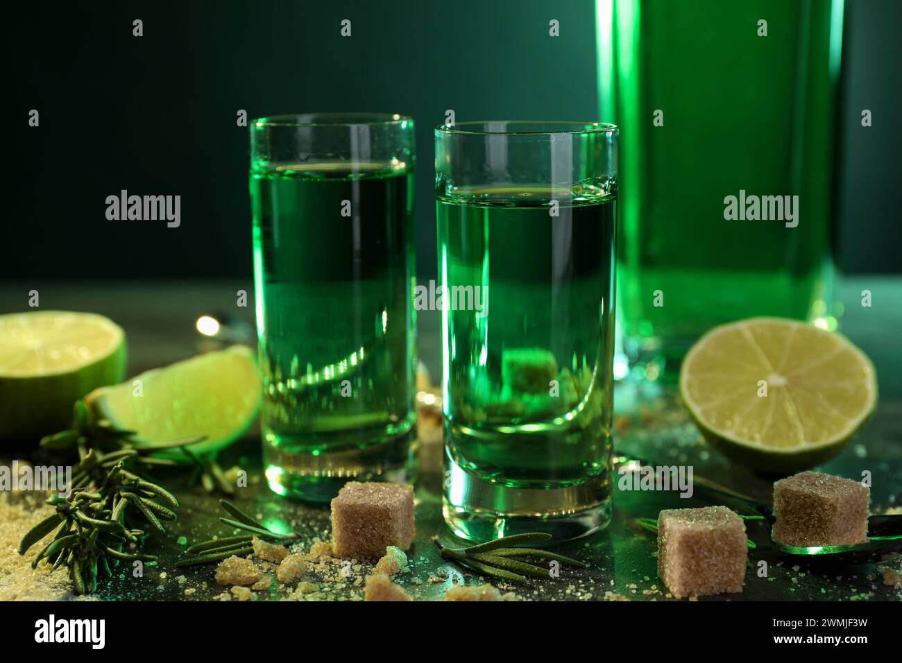 Absinthe in bicchieri da shot, zucchero di canna, lime e rosmarino sul tavolo, primo piano. Bevanda alcolica Foto Stock