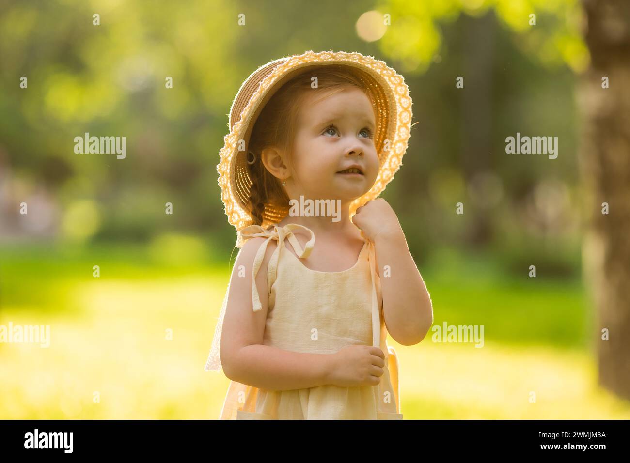 Una bambina carina con un abito di cotone e un cappello di paglia durante una passeggiata estiva. Foto di alta qualità Foto Stock