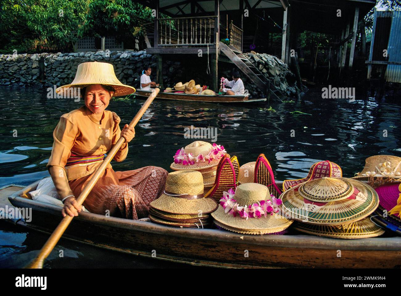 Donna tailandese sorridente con una canoa piena di cappelli di paglia; Damnoen Saduak, Thailandia Foto Stock